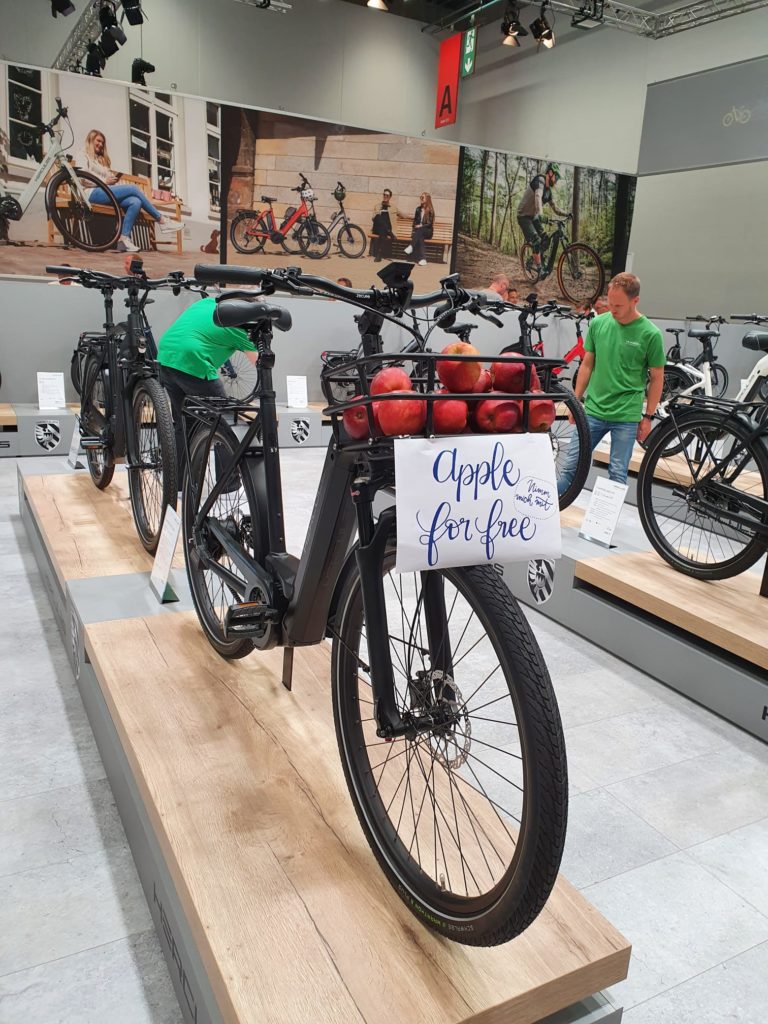 Ein matt schwarzes Hercules e-Bike steht auf einem Podest und der Fahrradkorb vorne ist mit Äpfeln befüllt