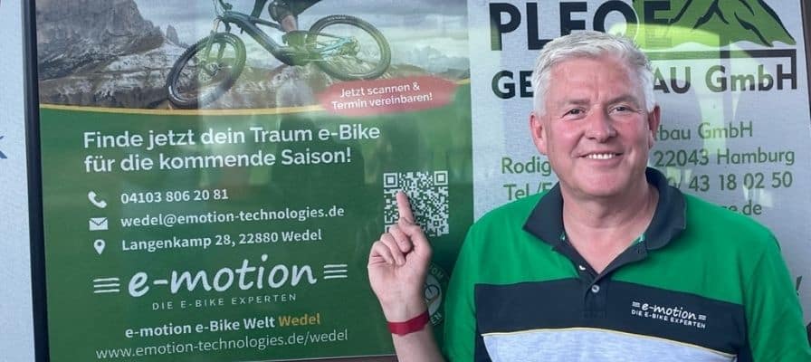 e-motion e-Bike Welt Wedel fördert den Sport und ein Mitarbeiter zeigt auf das Plakat