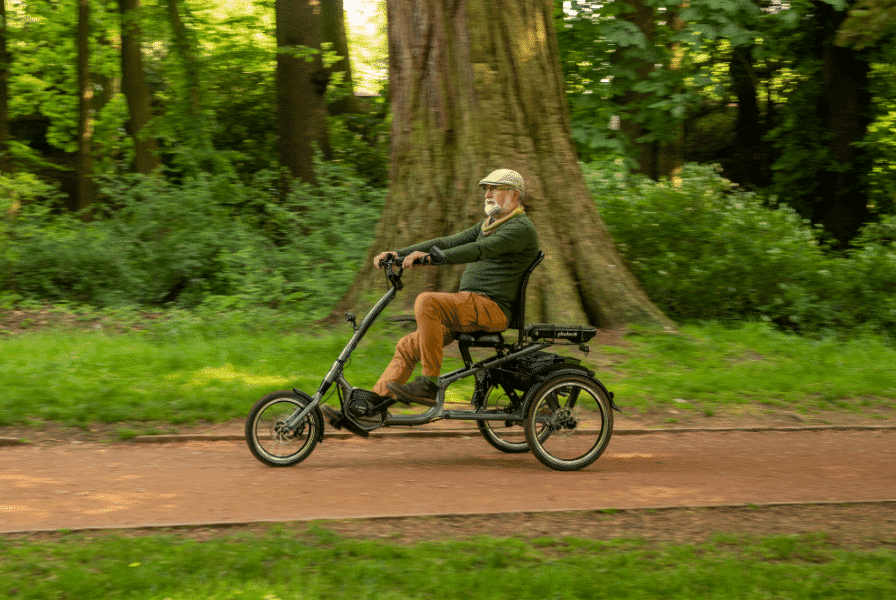 Ein älterer Herr fährt auf seinem Dreirad einen Waldweg entlang